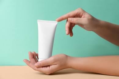 Tube of hand cream on beige table against turquoise background, closeup