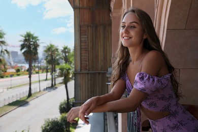Photo of Beautiful young woman standing on balcony, space for text