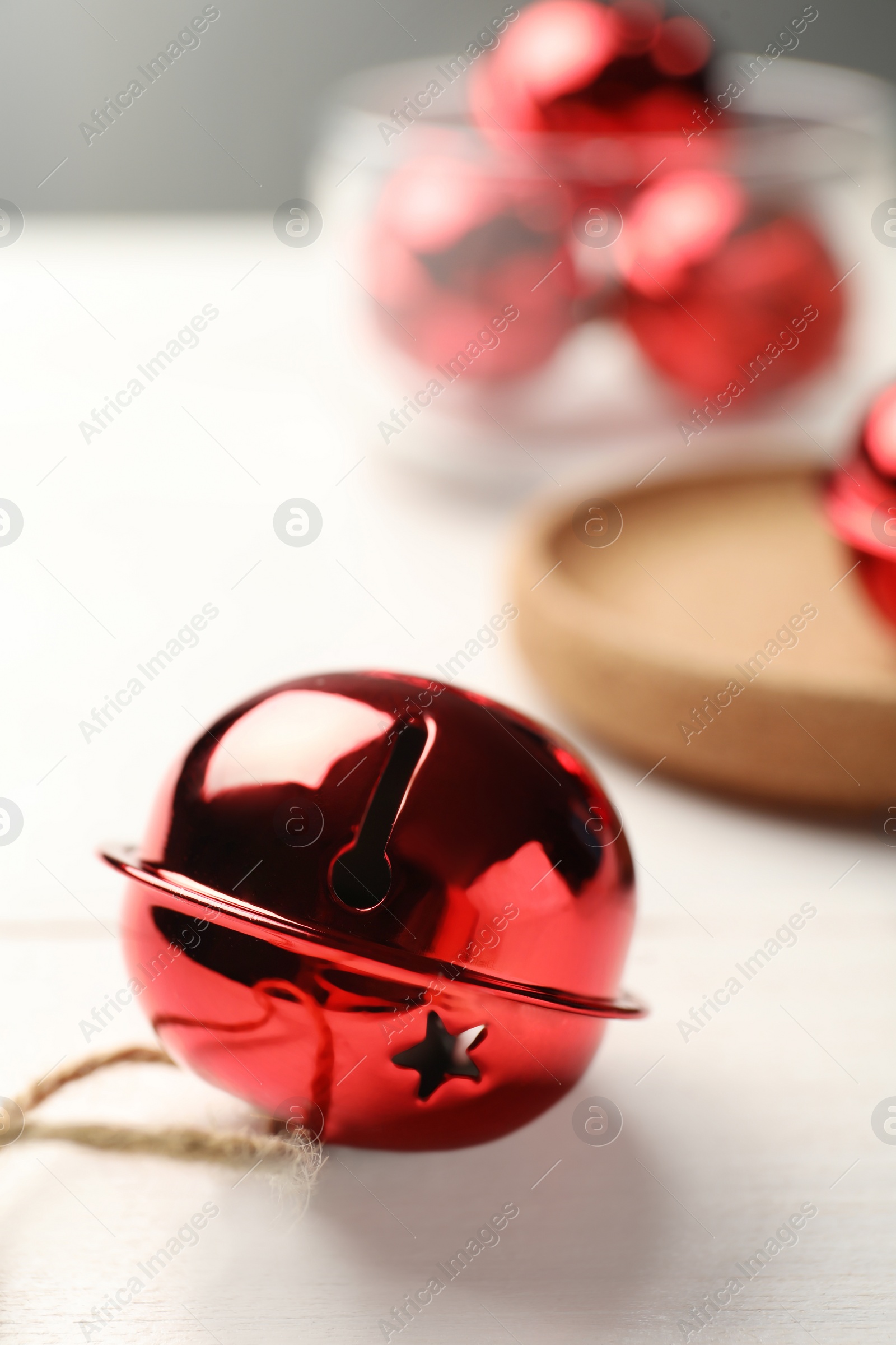 Photo of Red sleigh bell with rope on white table, closeup. Space for text