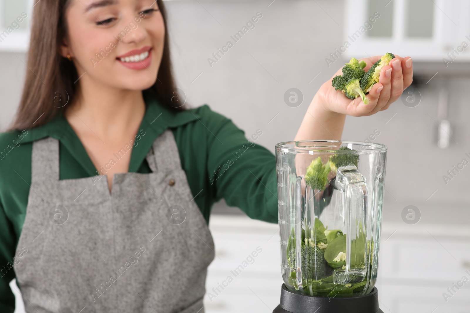 Photo of Woman adding broccoli into blender with ingredients for smoothie in kitchen, focus on hand