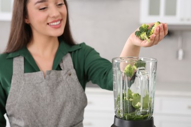 Woman adding broccoli into blender with ingredients for smoothie in kitchen, focus on hand