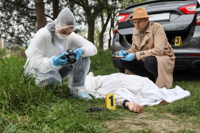 Photo of Investigator and criminologist working at crime scene with dead body outdoors