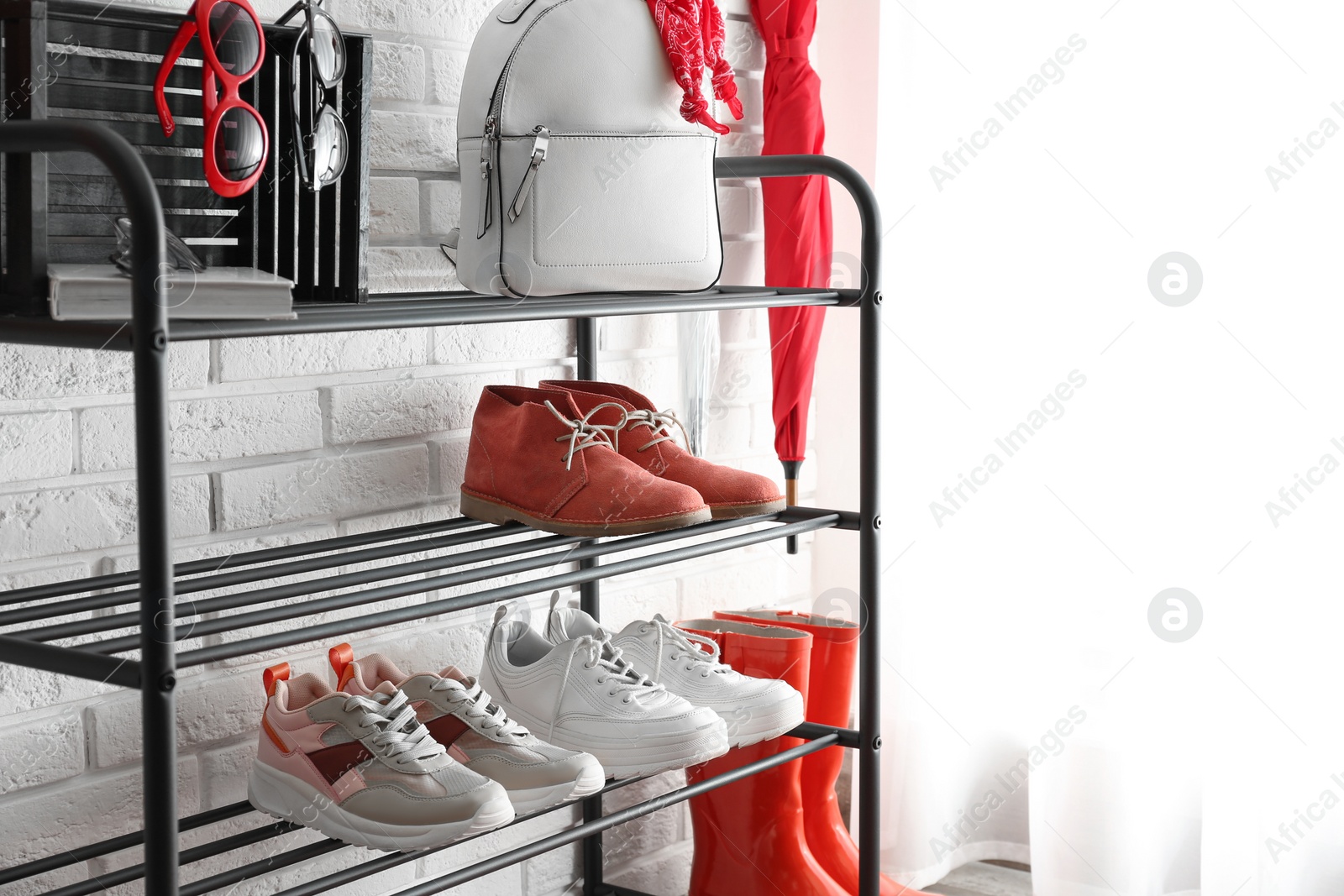 Photo of Shelving rack with stylish women's shoes and accessories near white brick wall indoors