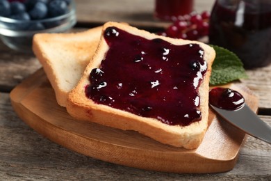 Photo of Delicious toasts with jam on wooden board, closeup