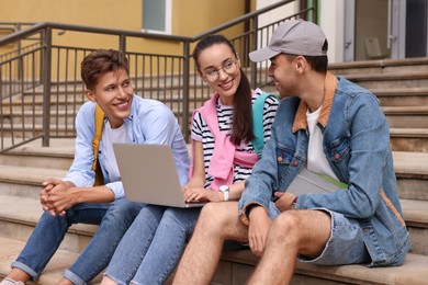 Photo of Happy young students studying together with laptop on steps outdoors