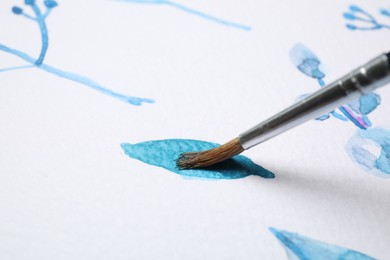 Photo of Painting leaf with blue watercolor on white paper, closeup