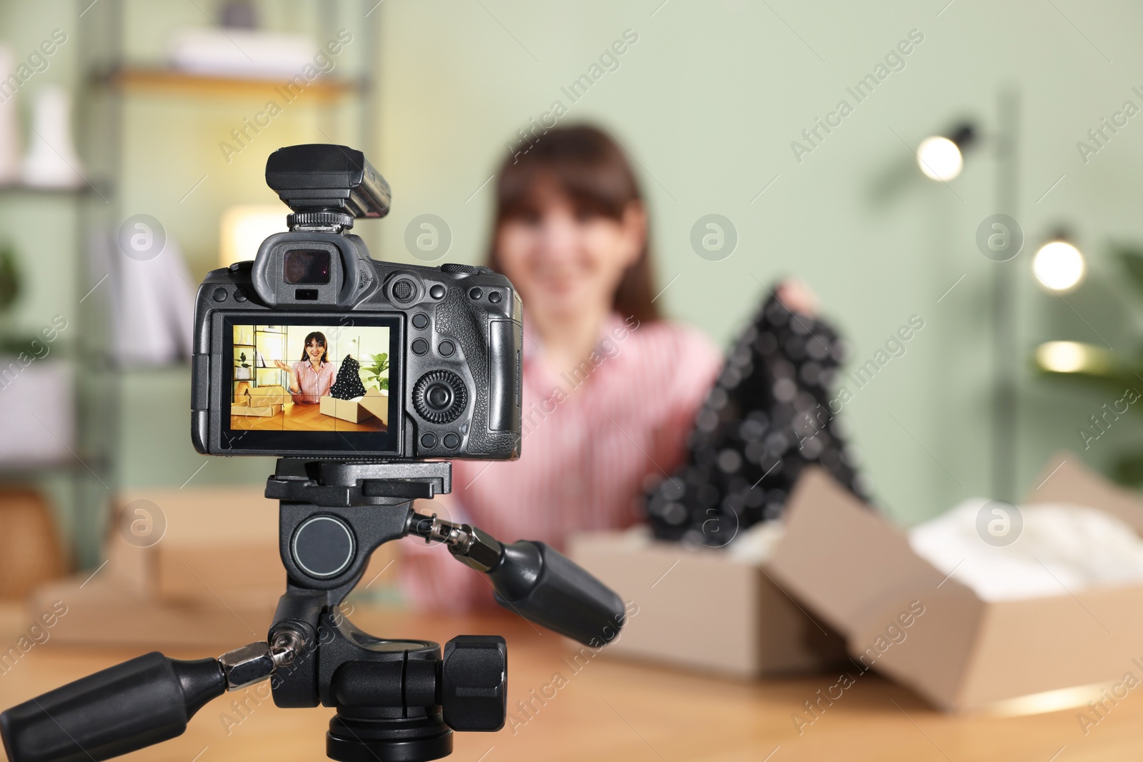 Photo of Fashion blogger recording video while talking about clothes at home, focus on camera