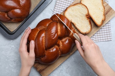 Photo of Woman cutting homemade braided bread at grey table, top view. Traditional Shabbat challah