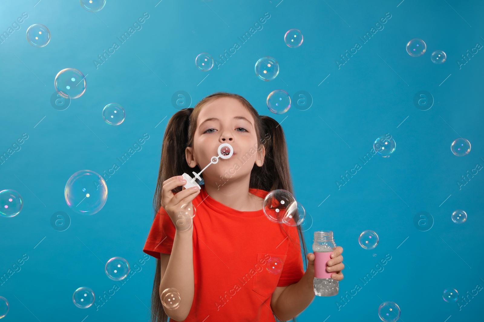 Photo of Little girl blowing soap bubbles on light blue background