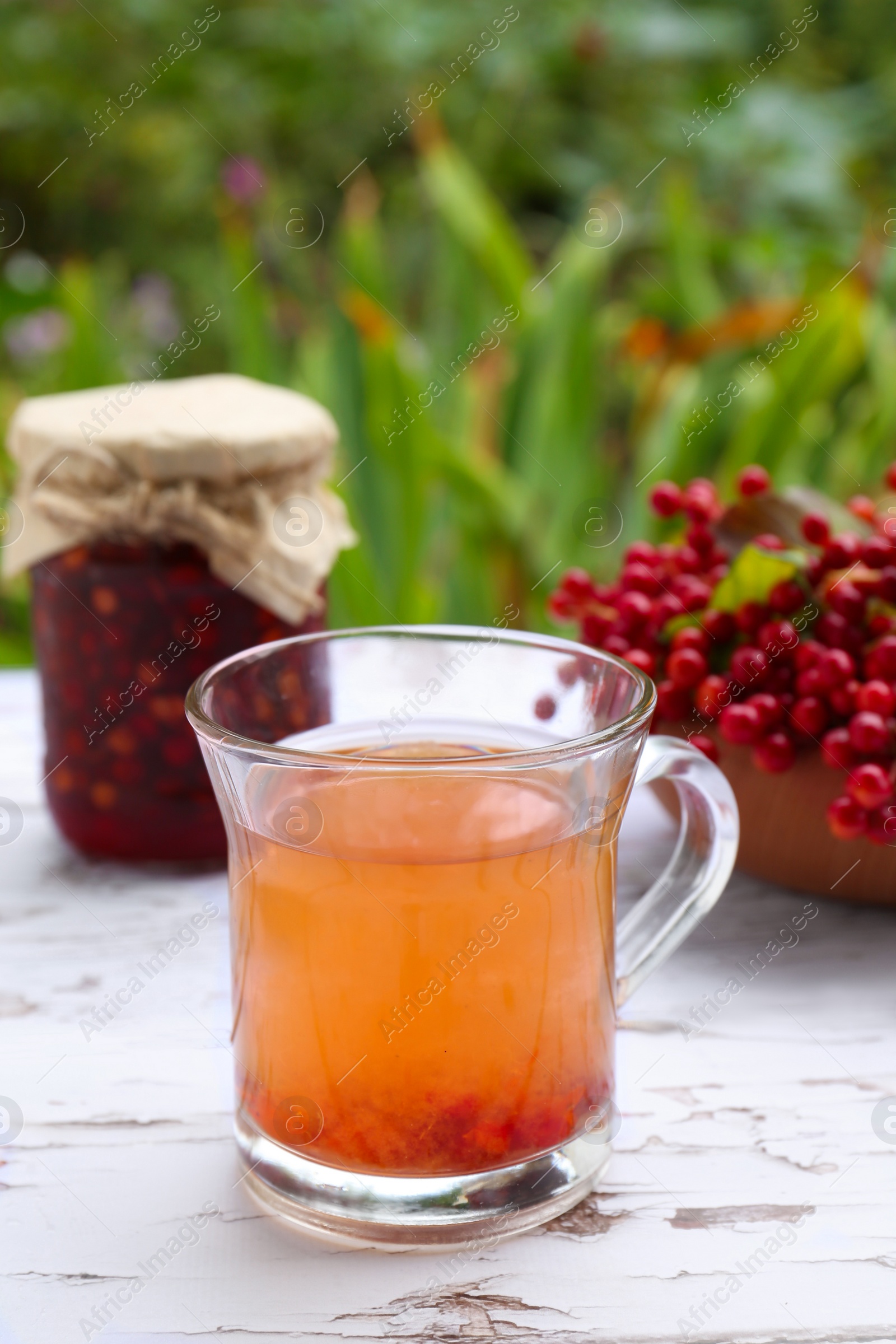 Photo of Cup of tea, jam and ripe viburnum berries on white wooden table outdoors