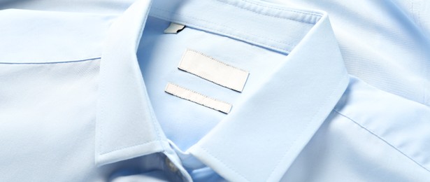 Blank clothing labels on light blue shirt, closeup. Banner design