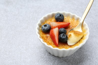 Delicious creme brulee with berries in bowl and spoon on grey textured table, closeup. Space for text