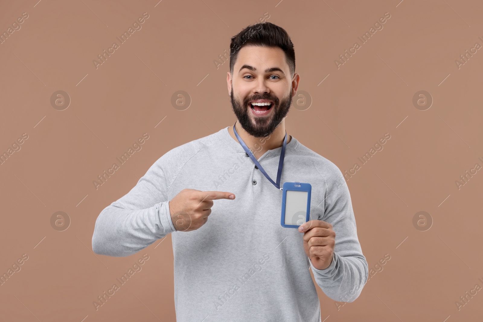 Photo of Emotional young man pointing at blank badge on beige background