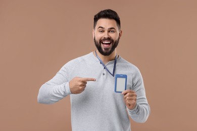 Emotional young man pointing at blank badge on beige background