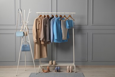 Rack with different stylish women`s clothes, shoes and bags near grey wall indoors