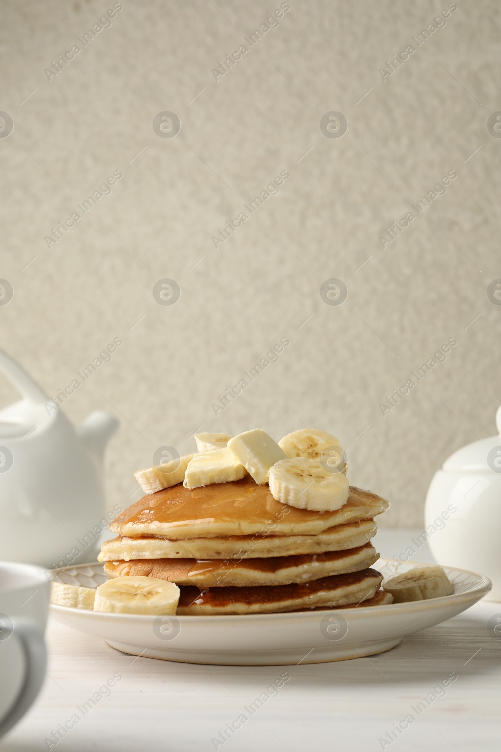 Photo of Delicious pancakes with bananas, honey and butter on white wooden table. Space for text