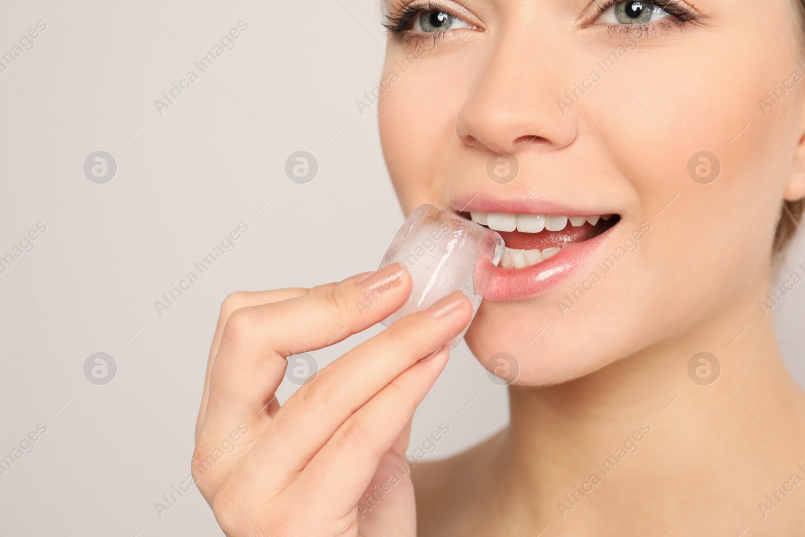 Photo of Young woman with ice cube on light background