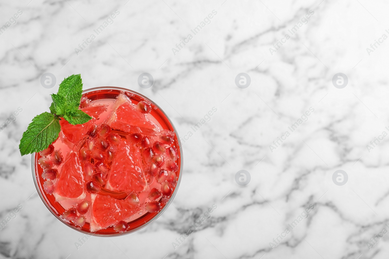 Photo of Glass of tasty refreshing cocktail with grapefruit and pomegranate on white marble background, top view. Space for text