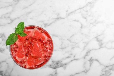 Glass of tasty refreshing cocktail with grapefruit and pomegranate on white marble background, top view. Space for text