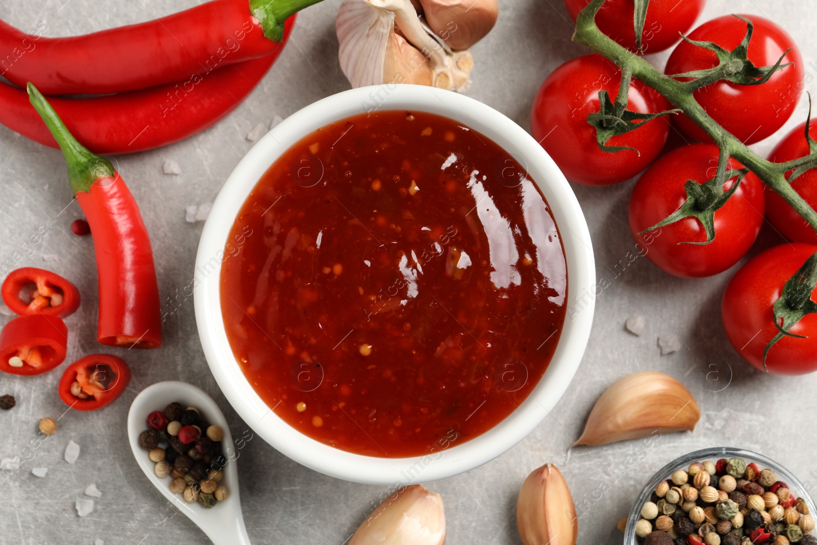 Photo of Spicy chili sauce and ingredients on grey table, flat lay