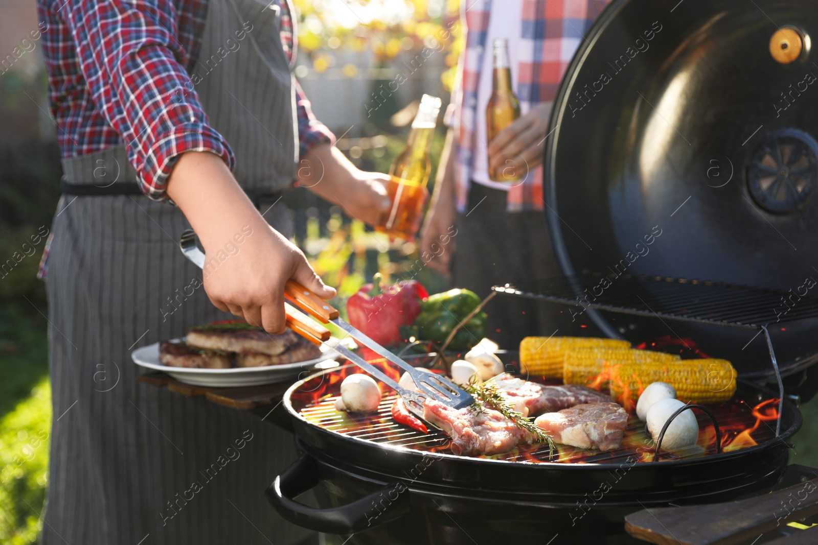 Photo of Man with drink cooking meat and vegetables on barbecue grill outdoors, closeup