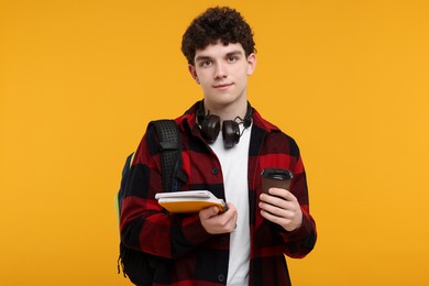 Portrait of student with backpack, headphones and notebooks on orange background