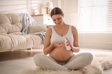 Photo of Young pregnant woman with cosmetic product at home