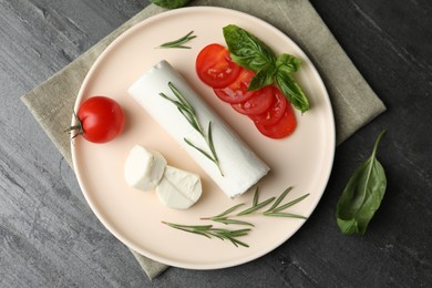 Photo of Delicious fresh goat cheese with tomatoes, basil and rosemary on grey table, flat lay