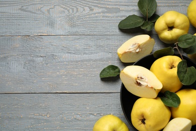 Photo of Fresh ripe organic quinces with leaves on grey wooden table, flat lay. Space for text