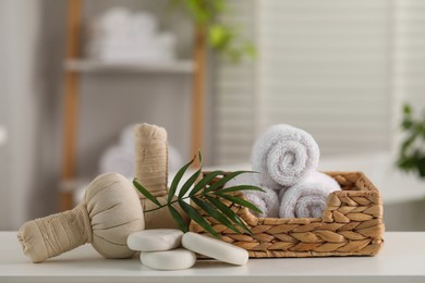 Spa composition. Towels, stones, herbal bags and palm leaves on white table in bathroom