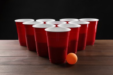 Photo of Plastic cups and ball for beer pong on wooden table against black background