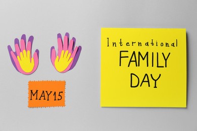 Photo of Card with text International Family Day near paper palms on grey background, flat lay