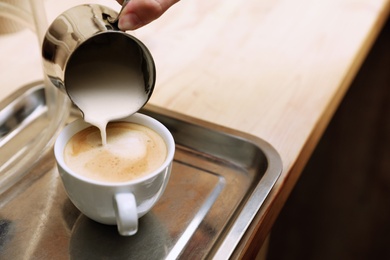 Barista adding milk to freshly brewed coffee on tray, closeup. Space for text