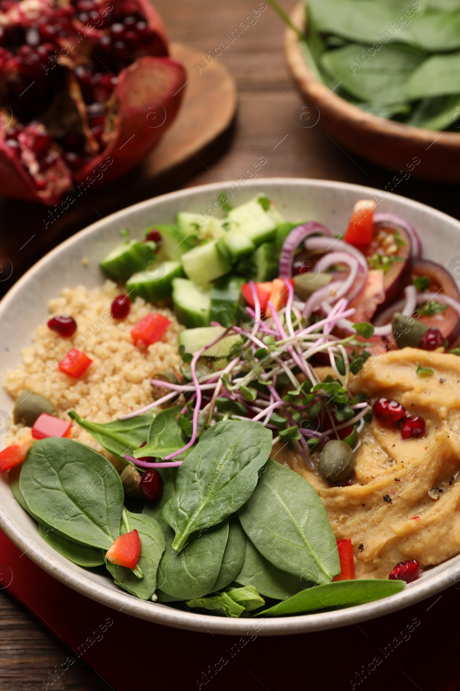 Photo of Delicious vegan bowl with cucumbers, spinach and bulgur on wooden table, closeup