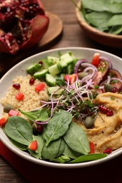 Photo of Delicious vegan bowl with cucumbers, spinach and bulgur on wooden table, closeup