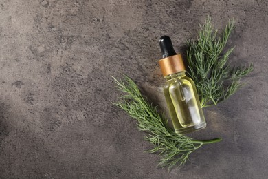 Bottle of essential oil and fresh dill on grey table, top view. Space for text