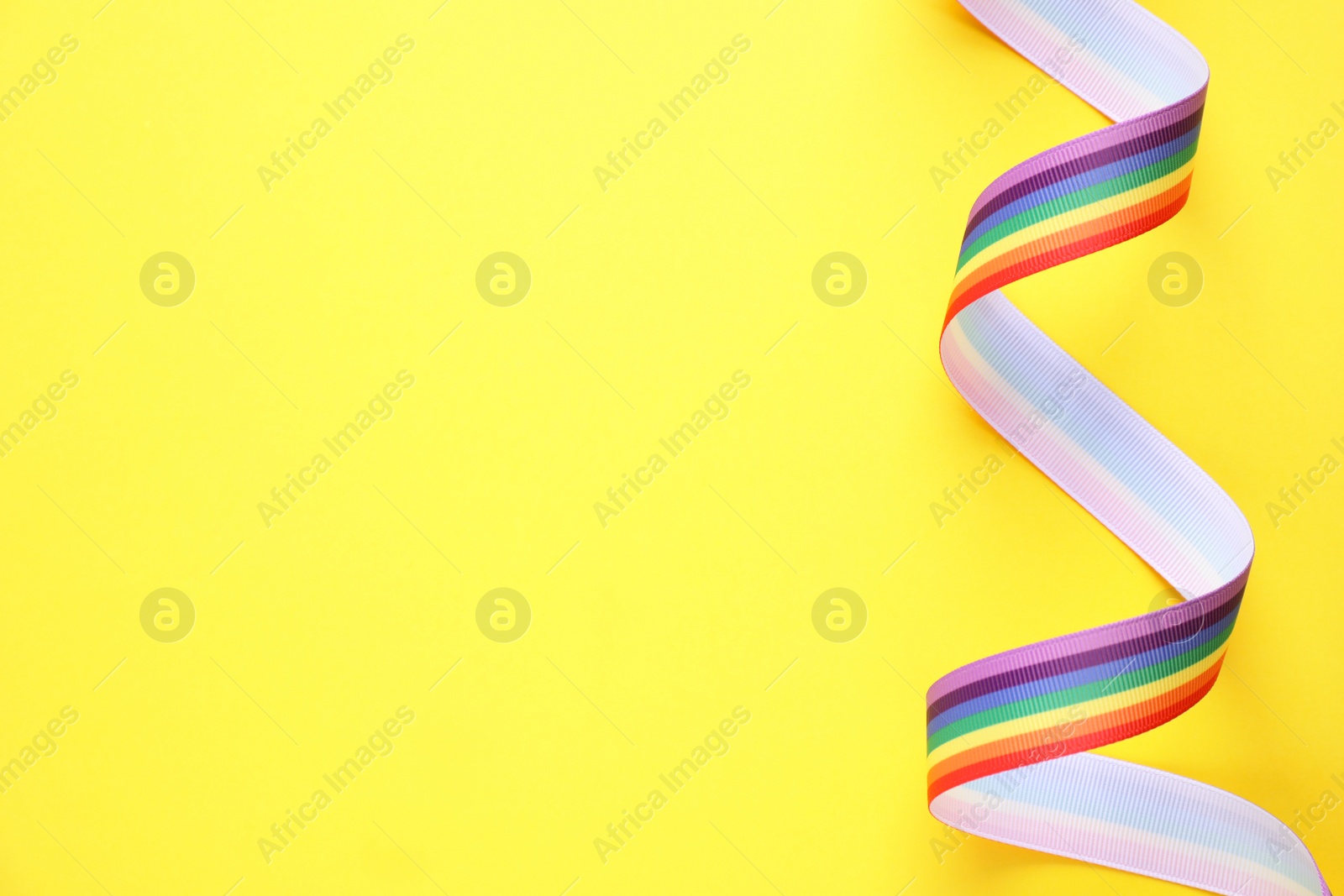 Photo of Top view of rainbow ribbon on yellow background, space for text. Gay symbol