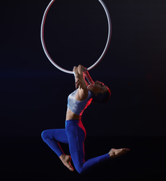 Photo of Young woman performing acrobatic element on aerial ring against dark background