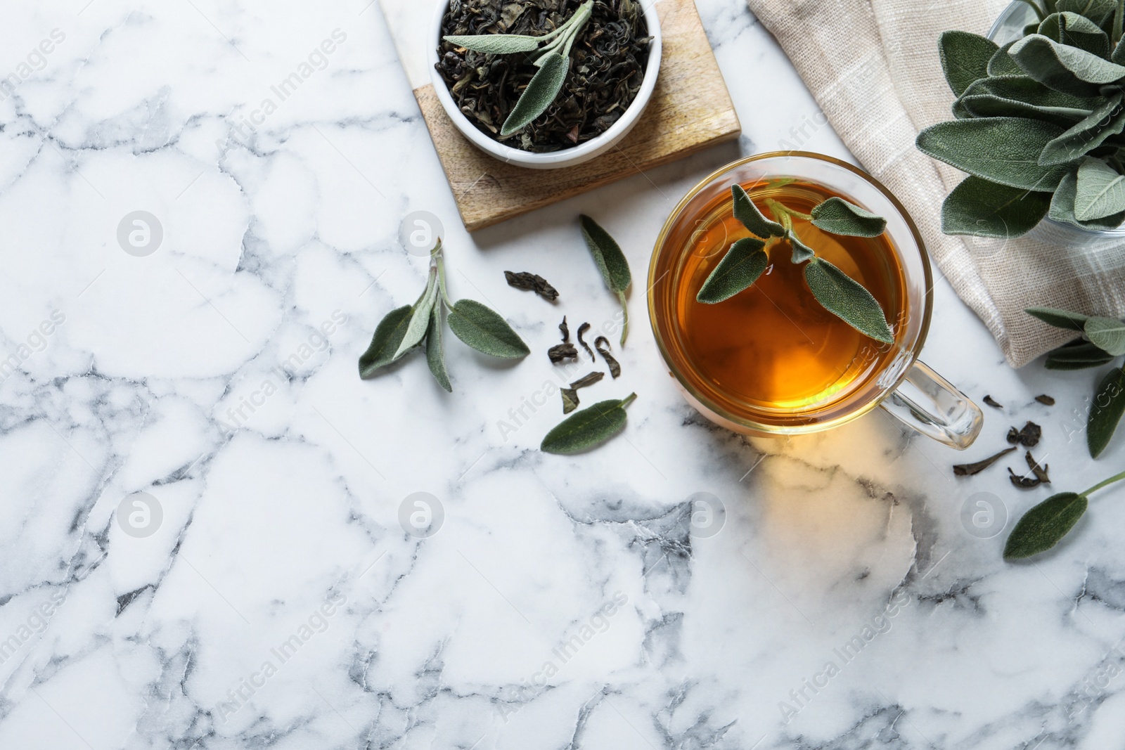 Photo of Cup of aromatic sage tea, dry and fresh leaves on white marble table, flat lay. Space for text