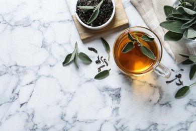 Photo of Cup of aromatic sage tea, dry and fresh leaves on white marble table, flat lay. Space for text