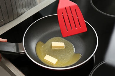 Photo of Woman stirring melted butter in frying pan on stove, closeup
