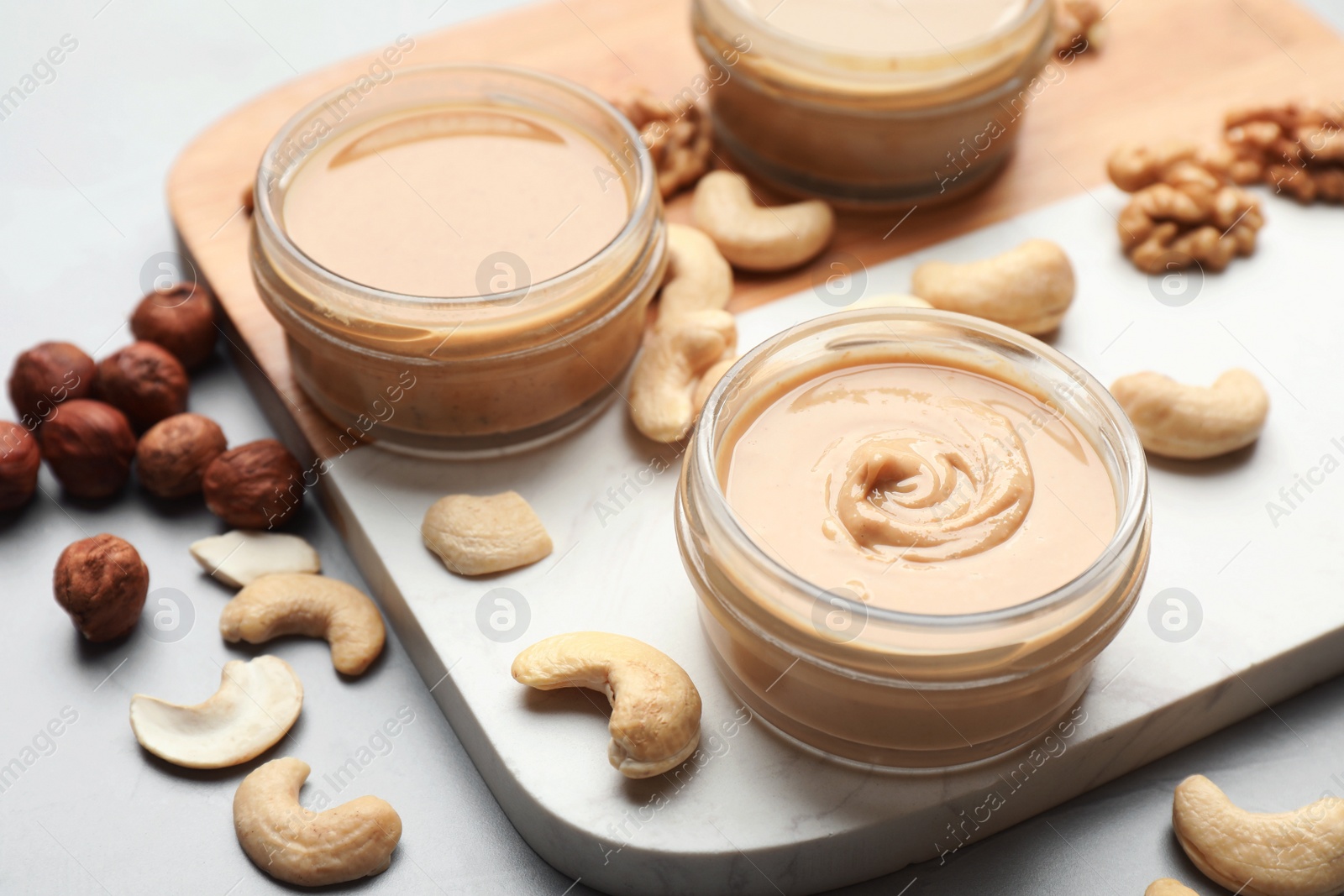 Photo of Different types of delicious nut butters and ingredients on light table, closeup