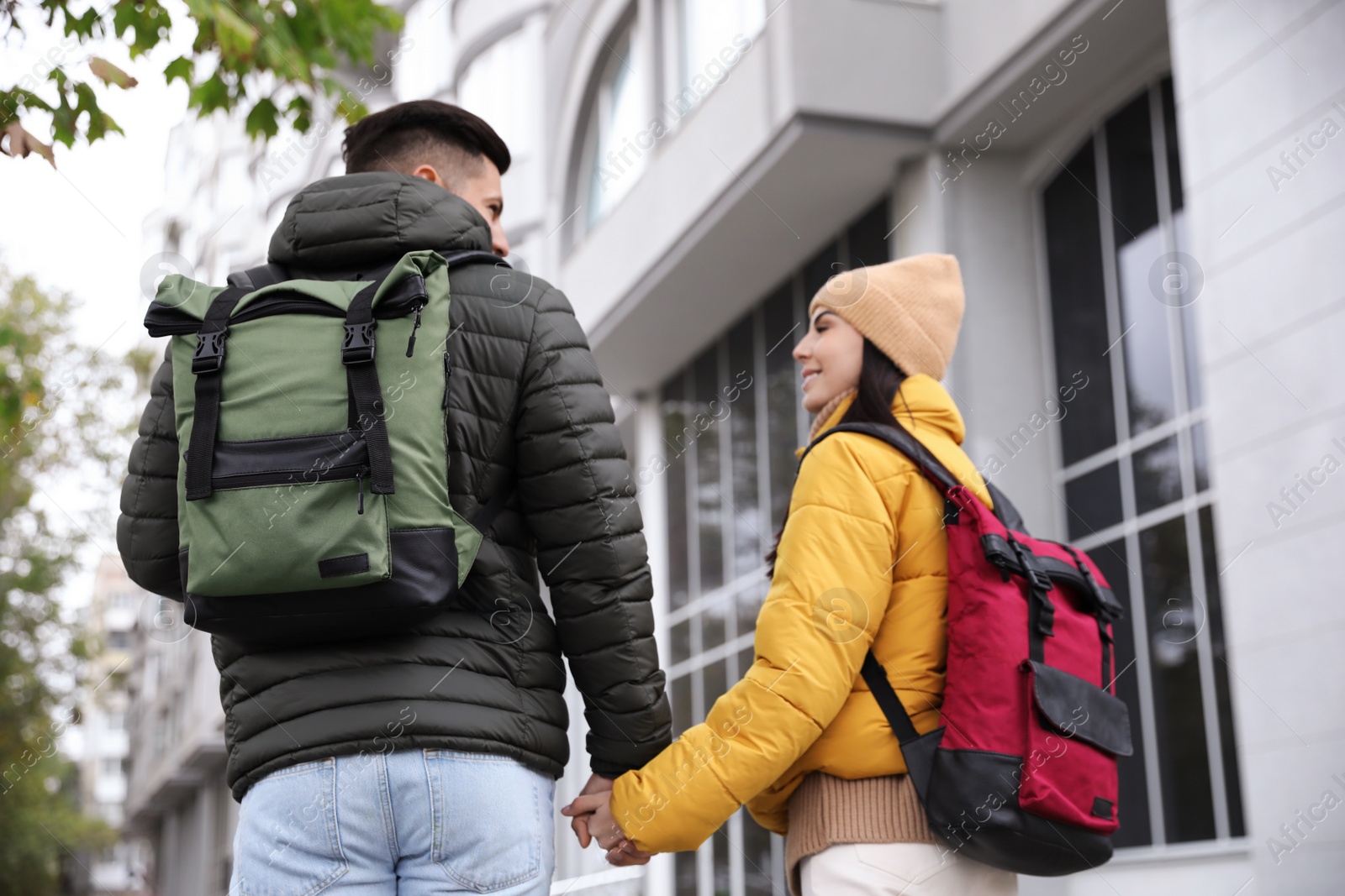 Photo of Couple with travel backpacks on city street, back view. Urban trip