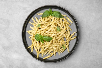 Plate of delicious trofie pasta with pesto sauce and basil leaves on light grey table, top view