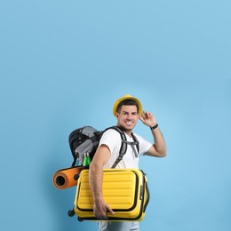 Male tourist with travel backpack and suitcase on turquoise background
