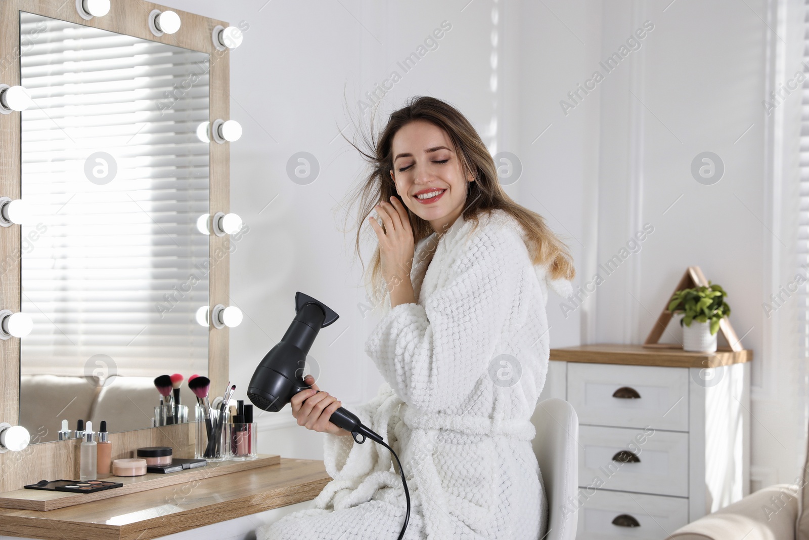 Photo of Beautiful young woman using hair dryer near mirror at home