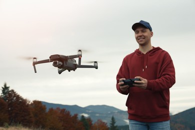 Photo of Young man operating modern drone with remote control in mountains