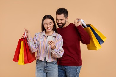 Happy couple with shopping bags and smartphone on beige background