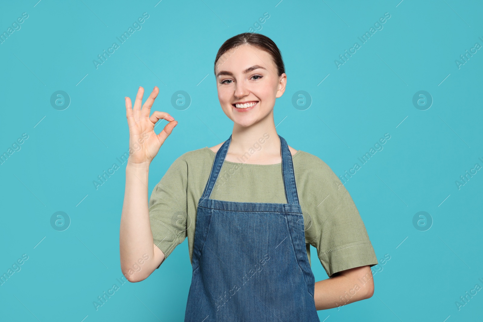 Photo of Beautiful young woman in clean denim apron on light blue background