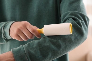 Man cleaning green sweatshirt with lint roller on light background, closeup